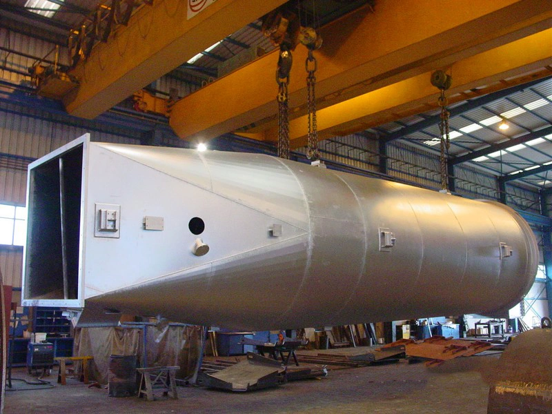 Large metal vessel suspended from overhead cranes in the workshop